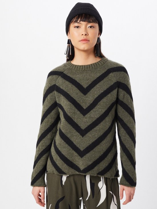Model met zwarte muts draagt een groene trui met zwarte chevron-strepen.