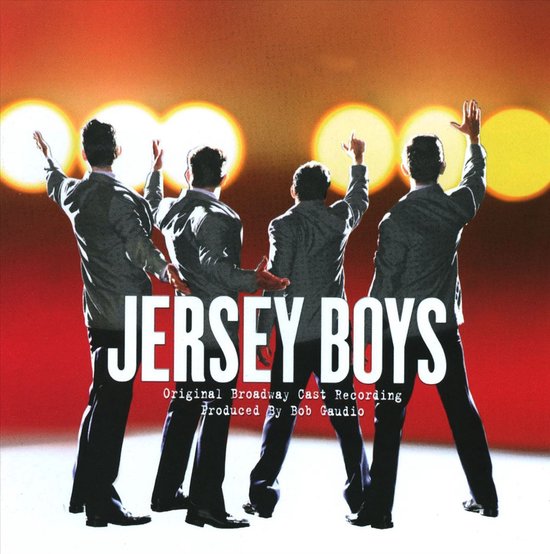Vier mannen in pakken, met hun rug naar de kijker, zwaaien met hun armen omhoog tegen een rode achtergrond met cirkels. Tekst: JERSEY BOYS.