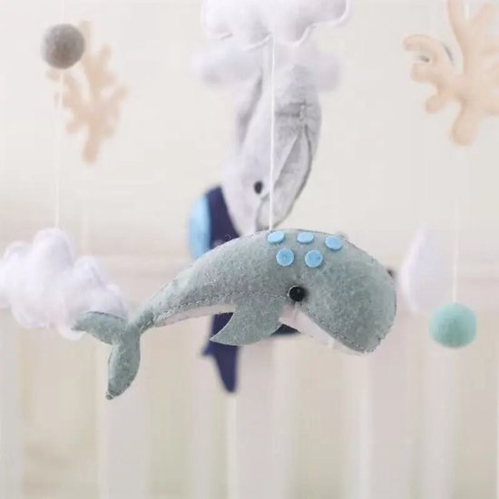 Close-up van een mintgroene vilten walvis met blauwe stippen, onderdelen van de mobiel: grijze walvis, wolken en koraal.