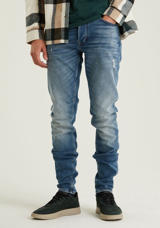 Man in een blauwe slim-fit jeans met lichte wassing en een gescheurd detail op de knie, gedragen met een geruit shirt.