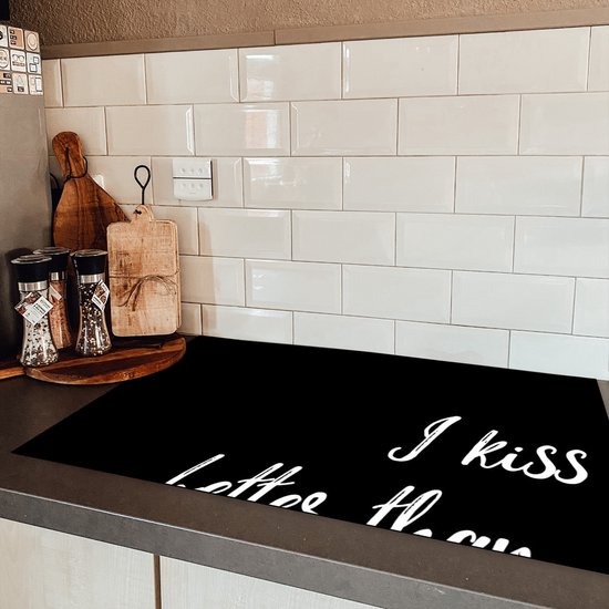 Zwarte kookplaatafdekking met witte tekst "I kiss better than I cook" in een keuken.