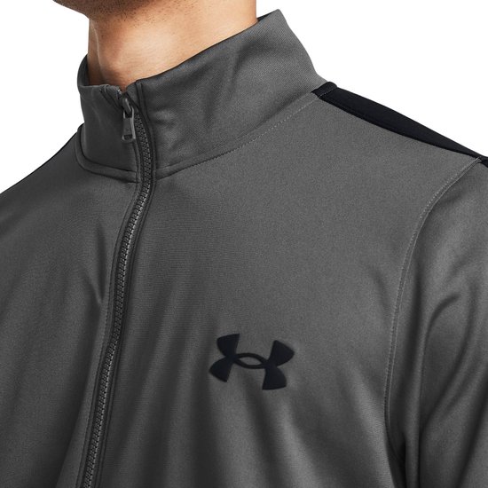 Grijs trainingsjack met zwarte strepen op de mouwen en een zwart Under Armour logo.