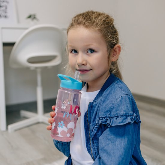 Une fille aux cheveux blonds boit dans une bouteille rose Minnie Mouse avec un bouchon bleu et une paille.