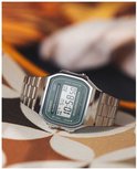 Zilverkleurig Casio horloge met groen digitaal display op een stoffen ondergrond met bloemenpatroon.
