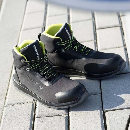 Paar zwarte Ardon werkschoenen met fluoriserende gele veters en voering, staand op een betegeld terras.