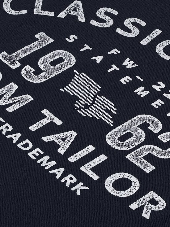Detail van een donkerblauwe opdruk met tekst 'CLASSIC BRAND FW 22 STATEMENT 19 62 TOM TAILOR EST. TRADEMARK'.