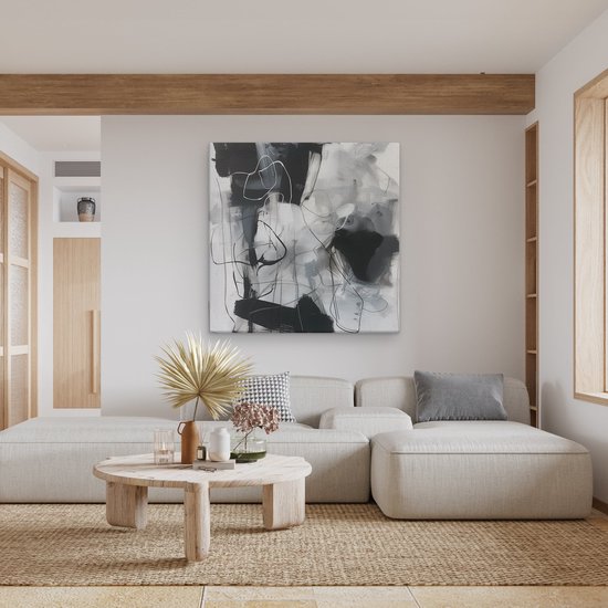 Abstract schilderij met zwarte, grijze en witte penseelstreken, boven een bank in een woonkamer.