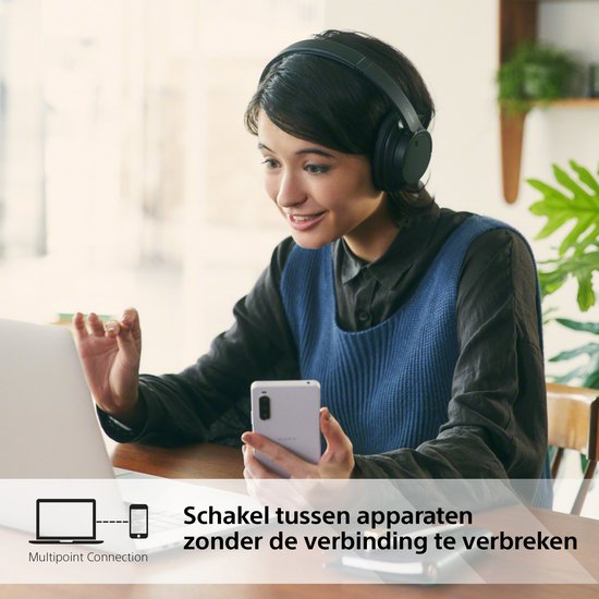 Vrouw met zwarte Sony koptelefoon, bij laptop en telefoon. 'Schakel tussen apparaten zonder de verbinding te verbreken'.