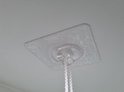 Transparante kleefhaak met touw aan een lichtgekleurd, gestructureerd plafond.