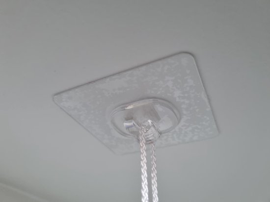 Transparante kleefhaak met touw aan een lichtgekleurd, gestructureerd plafond.