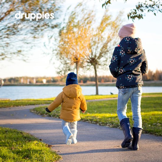 Twee kinderen lopen over een pad bij een meer in de herfst, een jongen in mosterdgeel en een meisje in een jas met bloemenprint.