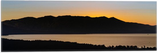 WallClassics - Vlag - Zon verdwijnend achter Berg onder Oranje Lucht - 60x20 cm Foto op Polyester Vlag