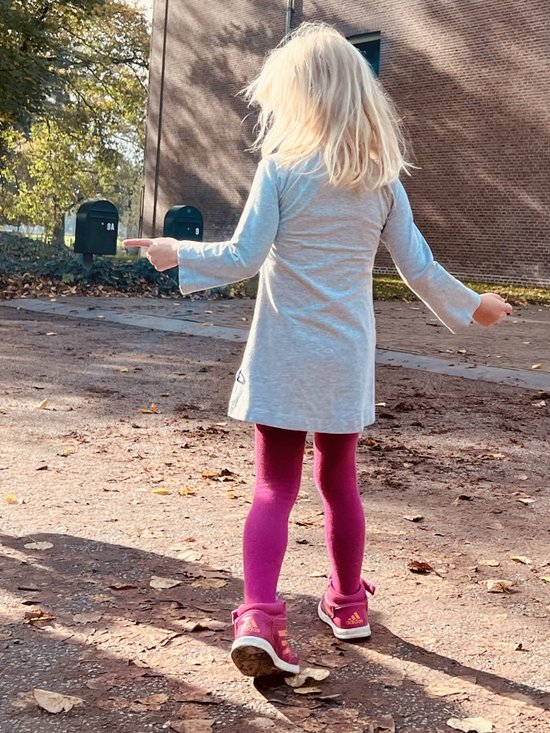 Jong meisje met blonde haren in een grijs jurkje, roze maillot en roze schoenen, wijzend.