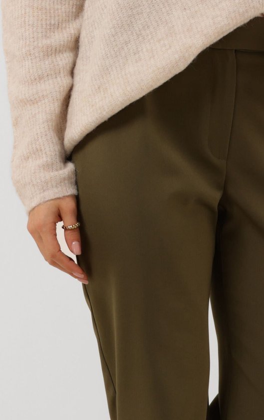 Detailopname van de hand van een model die een ring draagt en een donkergroene pantalon met wijde pijpen.