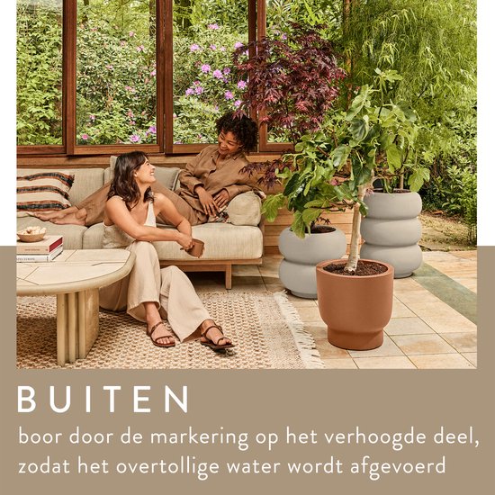 Twee witte, gestapelde bloempotten en een bruine pot met planten, in een overdekte buitenruimte.