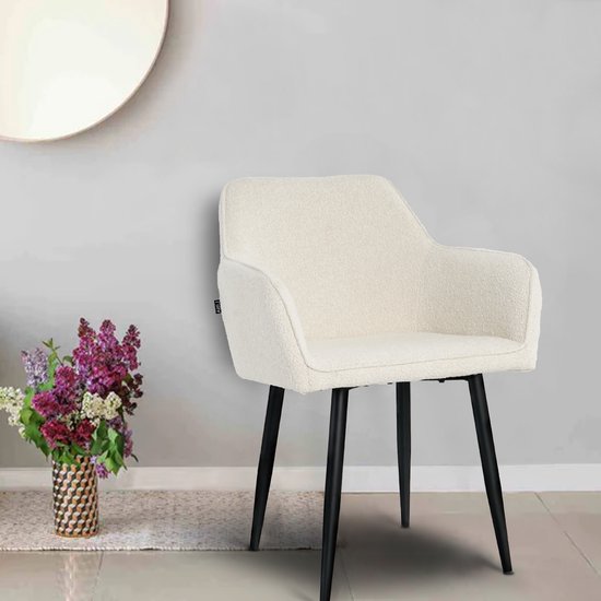 Crème boucle stoel met zwarte poten in een woonkamer, naast een vaas met bloemen.