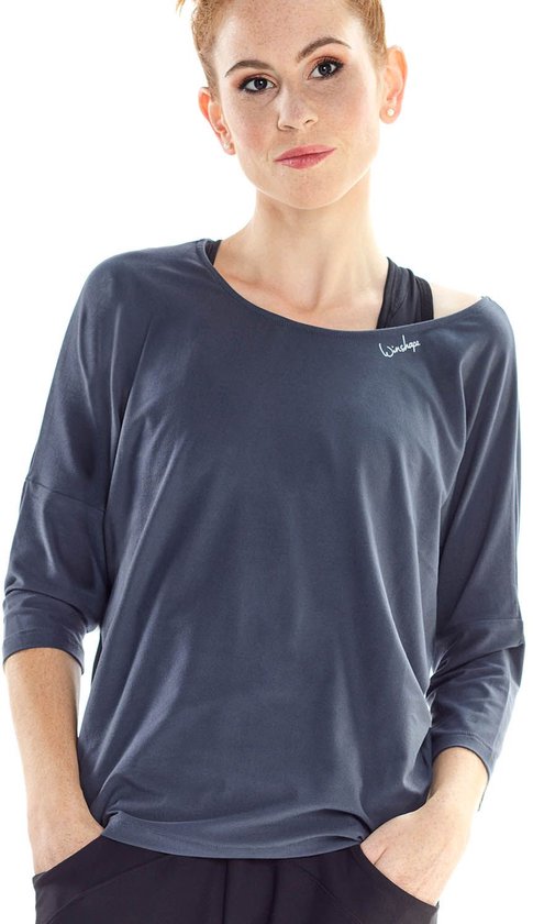 Model met rood haar in een antracietkleurig shirt met driekwart mouwen, met een sportbeha zichtbaar.
