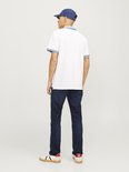 Man met witte polo, donkere jeans en cap.