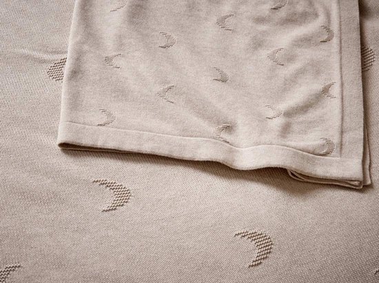 Close-up van een beige deken met een ingeweven patroon van maantjes.