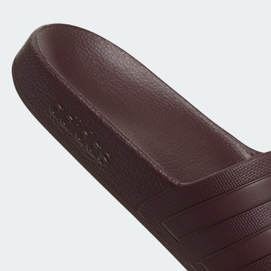 Gros plan sur la tong Adidas bordeaux avec le logo 'adidas' en creux sur la bride.