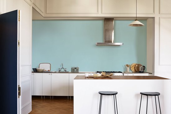 Keuken met lichtblauwe muur, witte keukenkastjes, kookeiland en barkrukken.