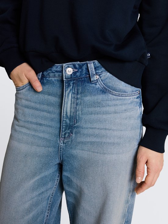 Detail van de tailleband van een wijde, lichtblauwe jeans met lichte wassing.