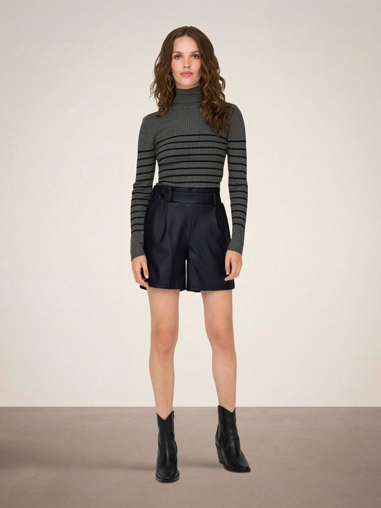 Vrouw met lang bruin golvend haar, draagt een gestreepte grijze coltrui en zwarte faux leren shorts.