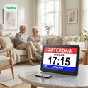Een oud stel dat op een bank zit, met een digitale klok op een salontafel die zaterdag 17:15, 10 januari toont.
