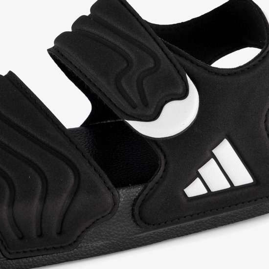 Close-up van zwarte Adidas Adilette sandalen voor kinderen met witte streeplogo's.
