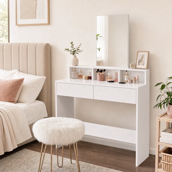 Moderne witte kaptafel met spiegel, twee lades en open vakken, met cosmetica, naast een bed in een slaapkamer.