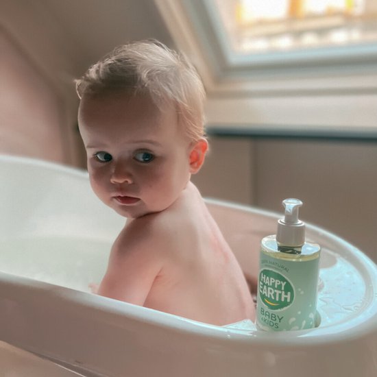 Baby in bad, naast een fles Happy Earth Baby & Kids Wash & Bath Gel.