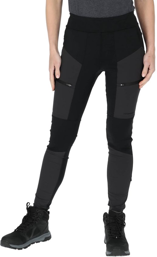 Femme en pantalon de randonnée noir avec empiècements gris foncé, poches zippées et chaussures de marche.
