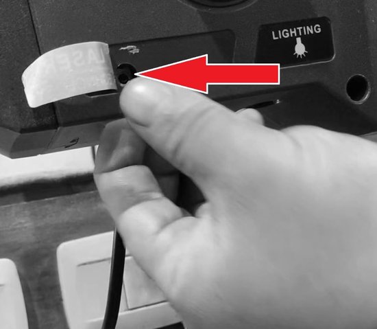 Hand die een kabel in de poort van een boormachine steekt, met "LIGHTING" sticker.