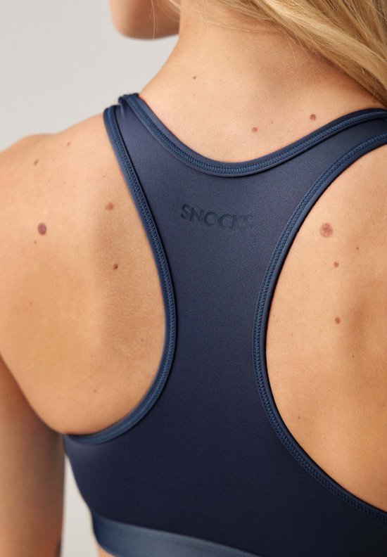Close-up van de SNOCKS-logo op de rug van een marineblauwe sportbeha met racerback. De naden van de bandjes zijn zichtbaar.