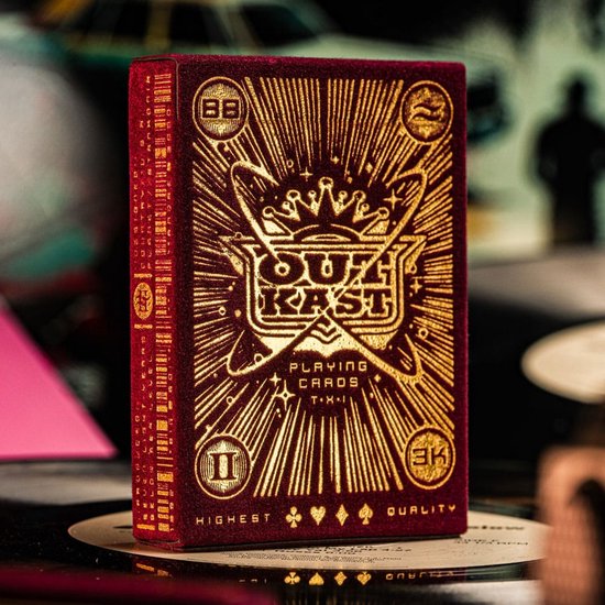Rood fluwelen speelkaarten doosje met gouden stralenkrans en kroon. 'OUTKAST PLAYING CARDS' in reliëf.