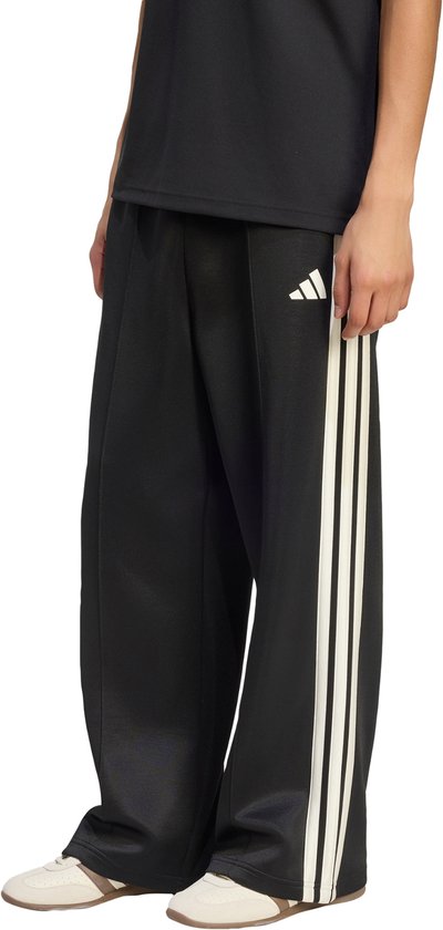 Zwarte wijde broek met witte adidas strepen en logo, gedragen met beige sneakers.