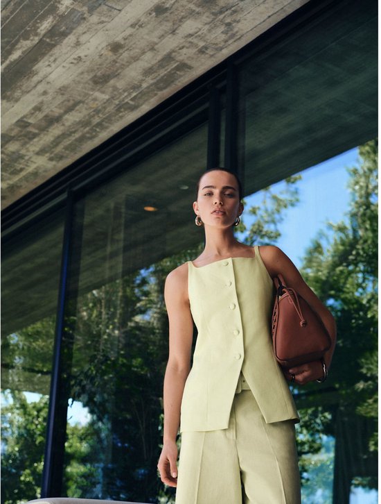 Model draagt een lichtgroene culotte en vierkante hals top, met een bruine tas.