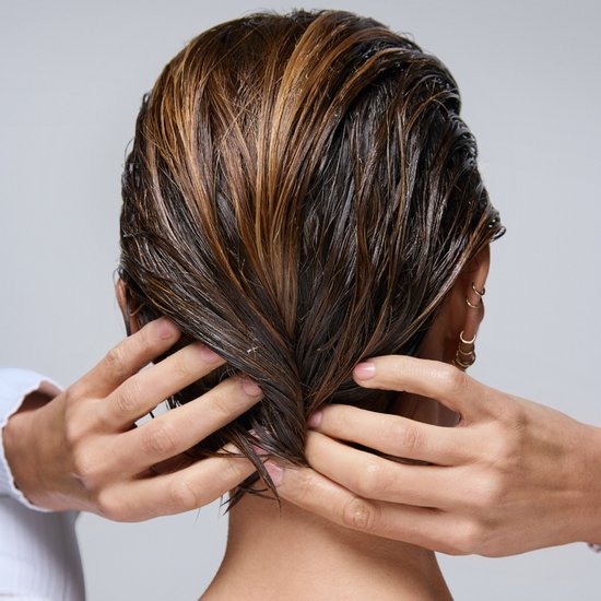Handen van een persoon die donker, nat haar met highlights stylen.
