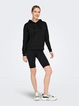 Model draagt een zwarte cropped hoodie en zwarte fietsbroek.