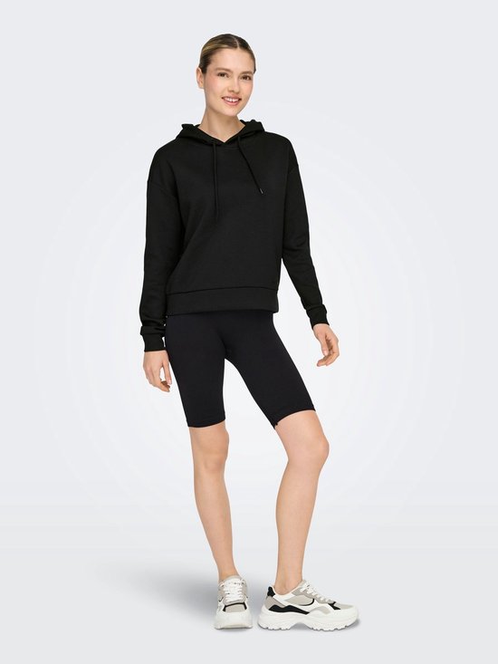 Model draagt een zwarte cropped hoodie en zwarte fietsbroek.