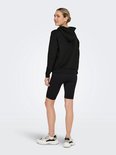 Model draagt een zwarte cropped hoodie en zwarte fietsbroek, van achteren gezien.