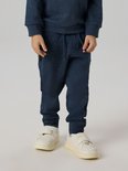 Onderlichaam van een jongen in een donkerblauw joggingbroek en witte sneakers.