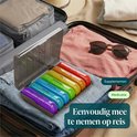 Boîte à pilules arc-en-ciel dans une valise ouverte, avec des vêtements et des lunettes de soleil à côté.