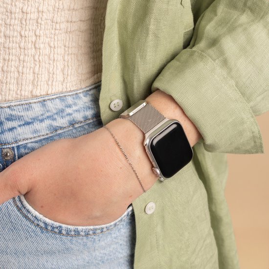 Close-up van een damespols met een smartwatch en Starlight Milanese bandje, nonchalant in een broekzak.