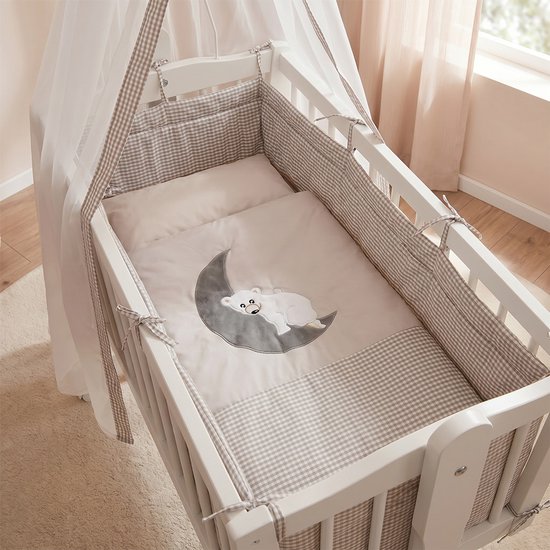 Wit kinderbed met hemel, plaid met beren- en maanmotief en ruitjespatroon.