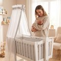 Wit kinderbed met hemel, ruitjespatroon en vrouw met baby.