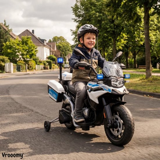 Een lachende jongen met helm rijdt op een witte politiemotor met zijwieltjes op straat.