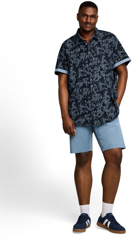 Man met een donkerblauw overhemd met korte mouwen en een lineair patroon, gedragen met een lichtblauwe short.