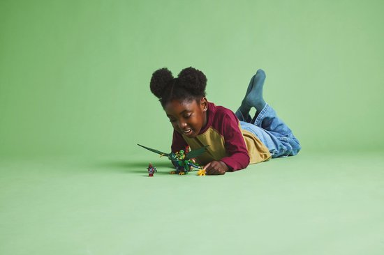 Jong meisje met afro-kapsel ligt op de grond en speelt met een groene LEGO draak en figuurtjes.