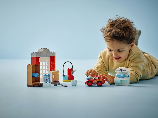 Jongetje met LEGO Duplo Cars set: rode Lightning McQueen, doktersgarage, gereedschap, op een blauwe ondergrond.